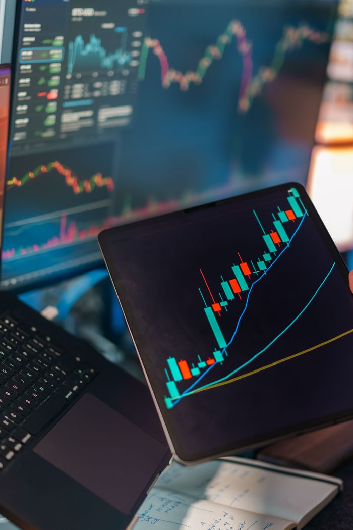 Services A tablet displaying a candlestick chart with a laptop screen showing stock market data for financial analysis.