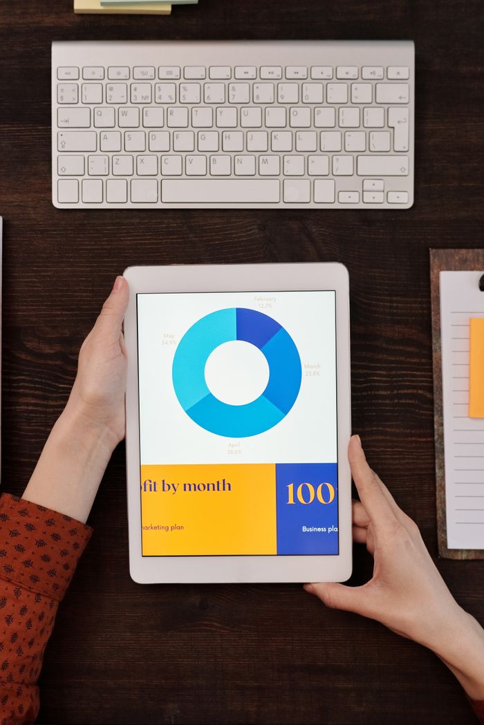 Services A person holds a tablet showing a business graph next to a keyboard on a wooden desk.