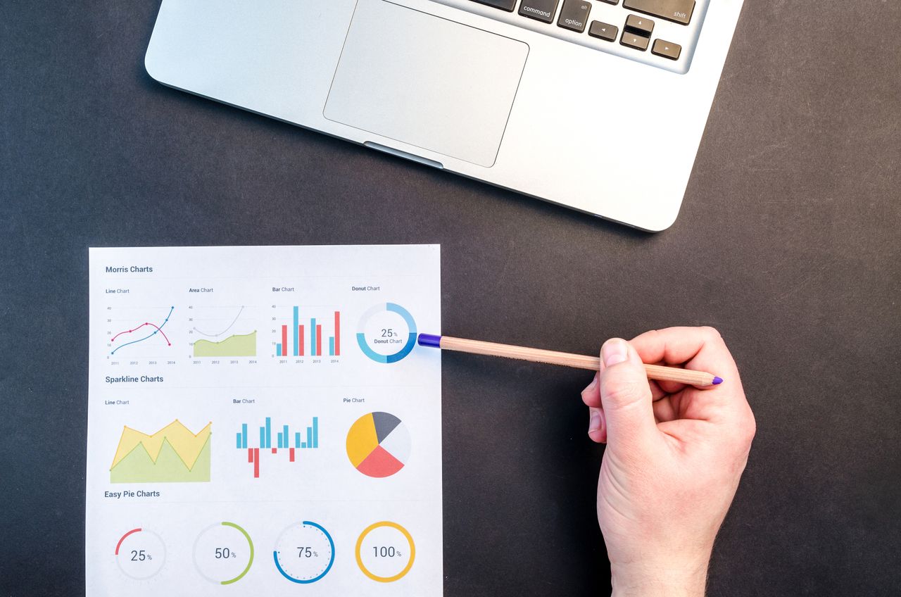 Services Hand holding pencil reviewing colorful data charts on desk with laptop.
